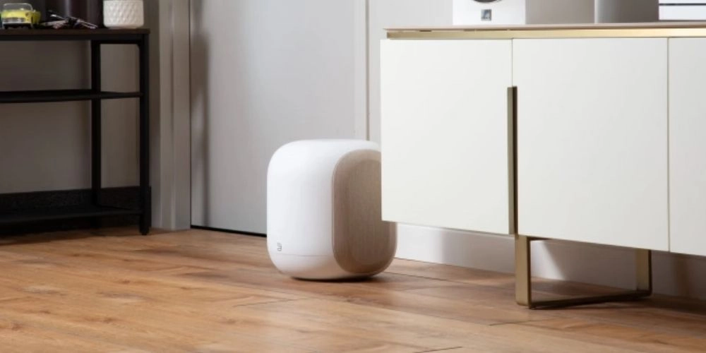 Caisson de basses Bluesound PULSE SUB Blanc-Tan posé au sol dans une entrée avec parquet et meuble bas