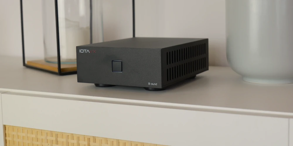 IOTAVX B:ound noir posé sur une étagère blanche, vu de trois quarts avec ses ouïes de ventilation latérales