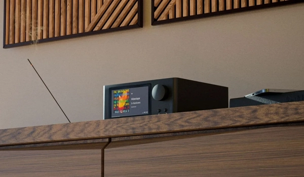 NAD C 700 V2 vu en angle sur une étagère en bois, écran couleur allumé et smartphone posé à côté.
