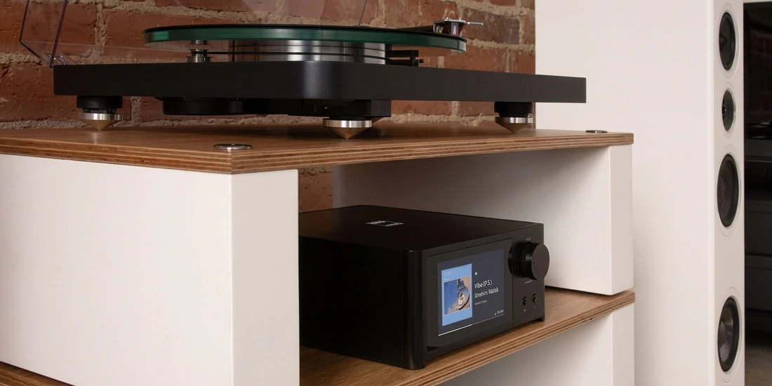 NAD C 700 V2 rangé sur une étagère, sous une platine vinyle et à côté d'une enceinte colonne à pavillon.