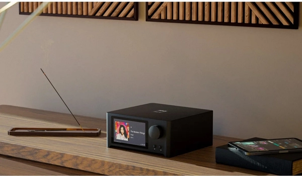 Amplificateur NAD C 700 V2 installé sur une étagère en bois, smartphone posé à proximité pour le contrôle BluOS.