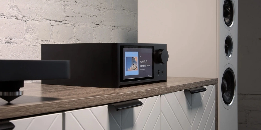 Amplificateur NAD C 700 V2 posé sur un meuble bas, à côté d'une platine vinyle et d'une enceinte colonne.