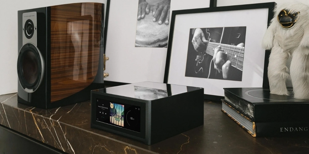 Amplificateur NAD M10 V3 posé sur une console en marbre, entre une enceinte bibliothèque en bois et des cadres photo.