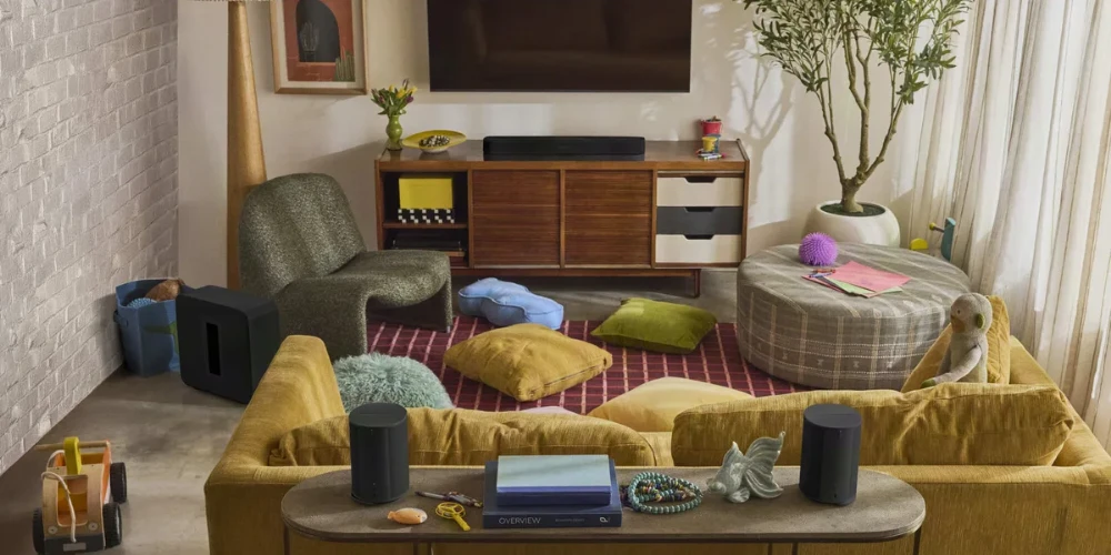 Salon avec la Sonos Beam Ultra noire sous un téléviseur mural, un caisson de basses et deux enceintes surround sur une table