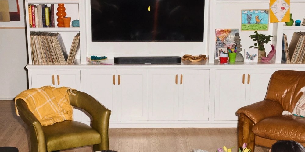Sonos Beam Ultra noire posée sur une bibliothèque blanche sous un téléviseur, entre vinyles et livres de famille.