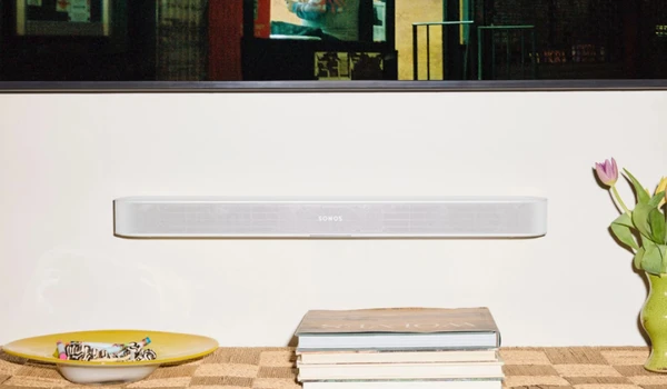 Sonos Beam Ultra blanche fixée sous un téléviseur mural, avec des fleurs et des livres posés sur un meuble.
