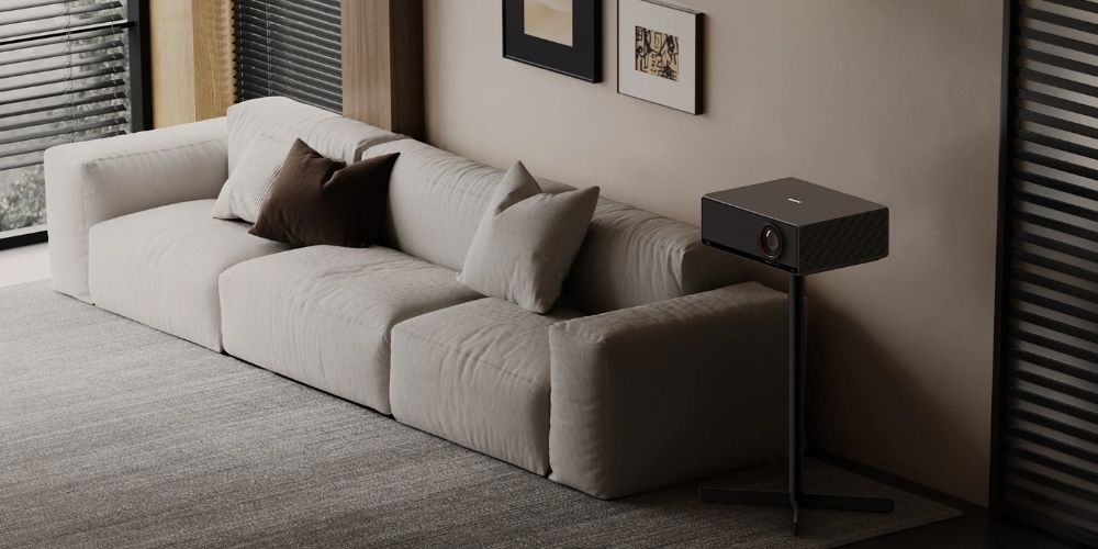 Xgimi Pied de Sol Titan positionné en salon à côté d'un canapé, supportant le projecteur Titan à hauteur optimale de projection