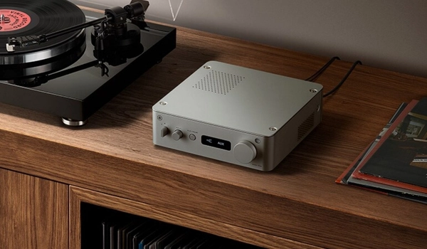 Yamaha WXA-70A en finition argent posé sur un meuble en bois, câblé à une platine vinyle visible à l'arrière-plan.